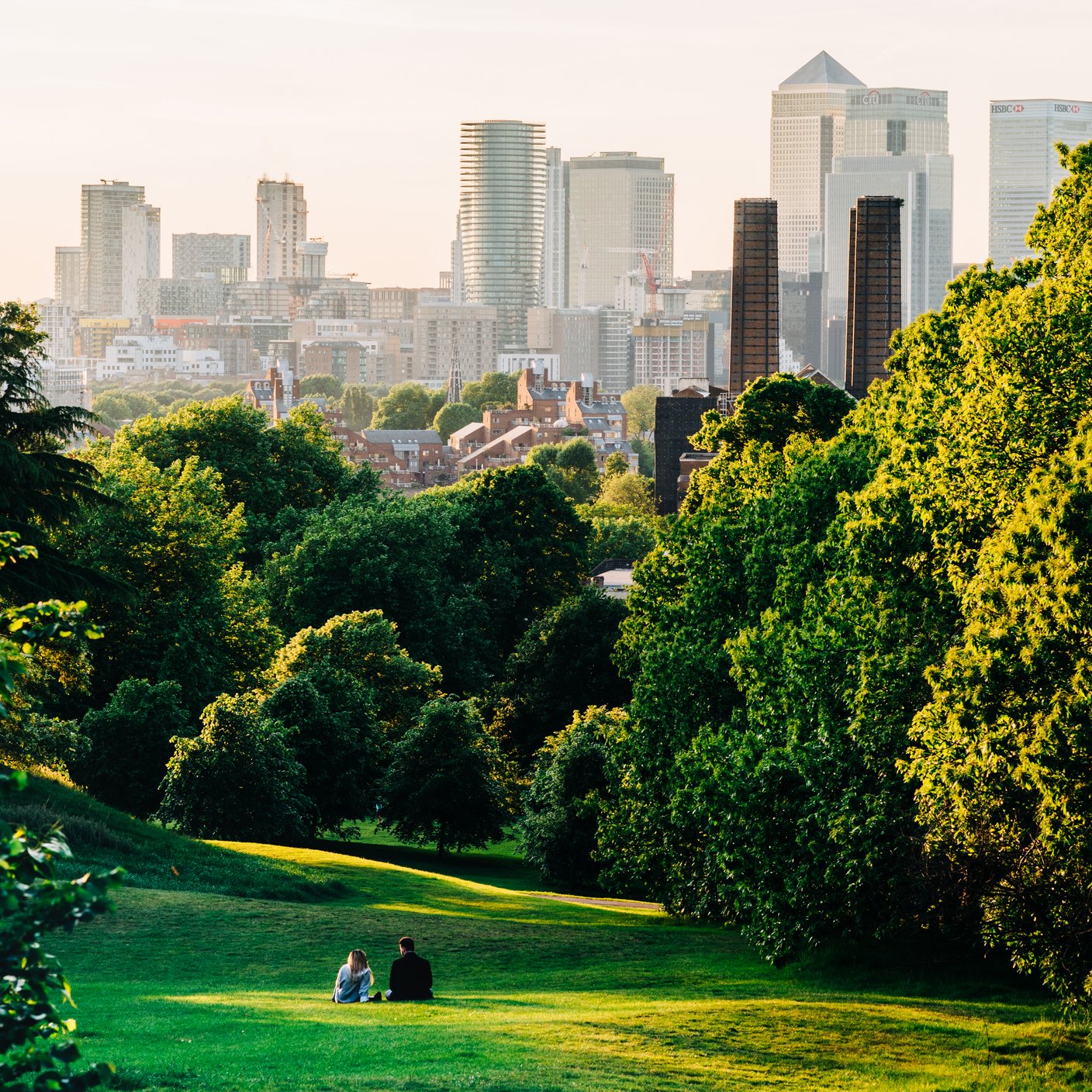 A couple sit in Greenwich Park, London looking the Canary .Wharf skyline