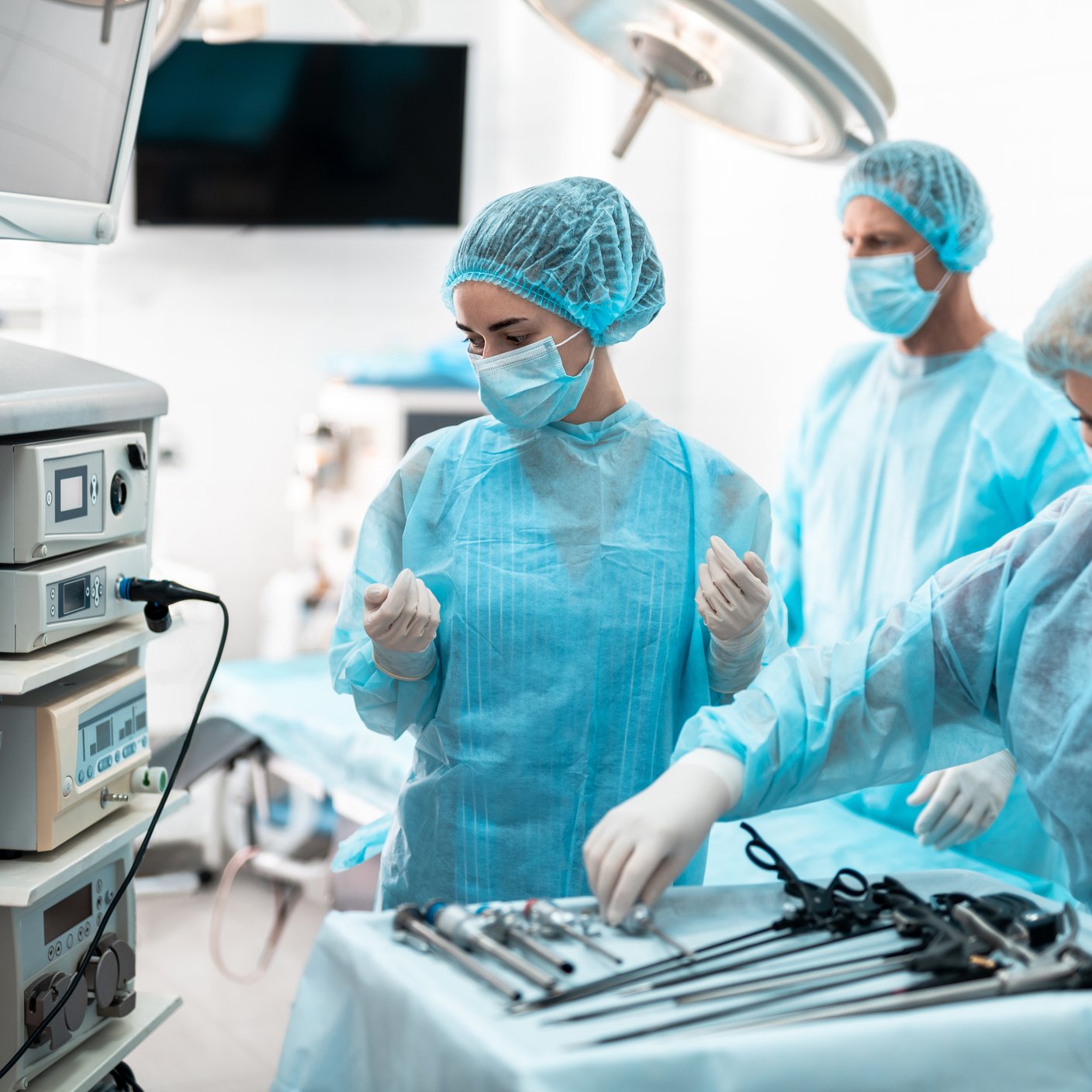 Waist up portrait of nurses in protective masks and sterile gloves checking laparoscopic instruments and medical equipment while surgeon standing behind them on blurred background