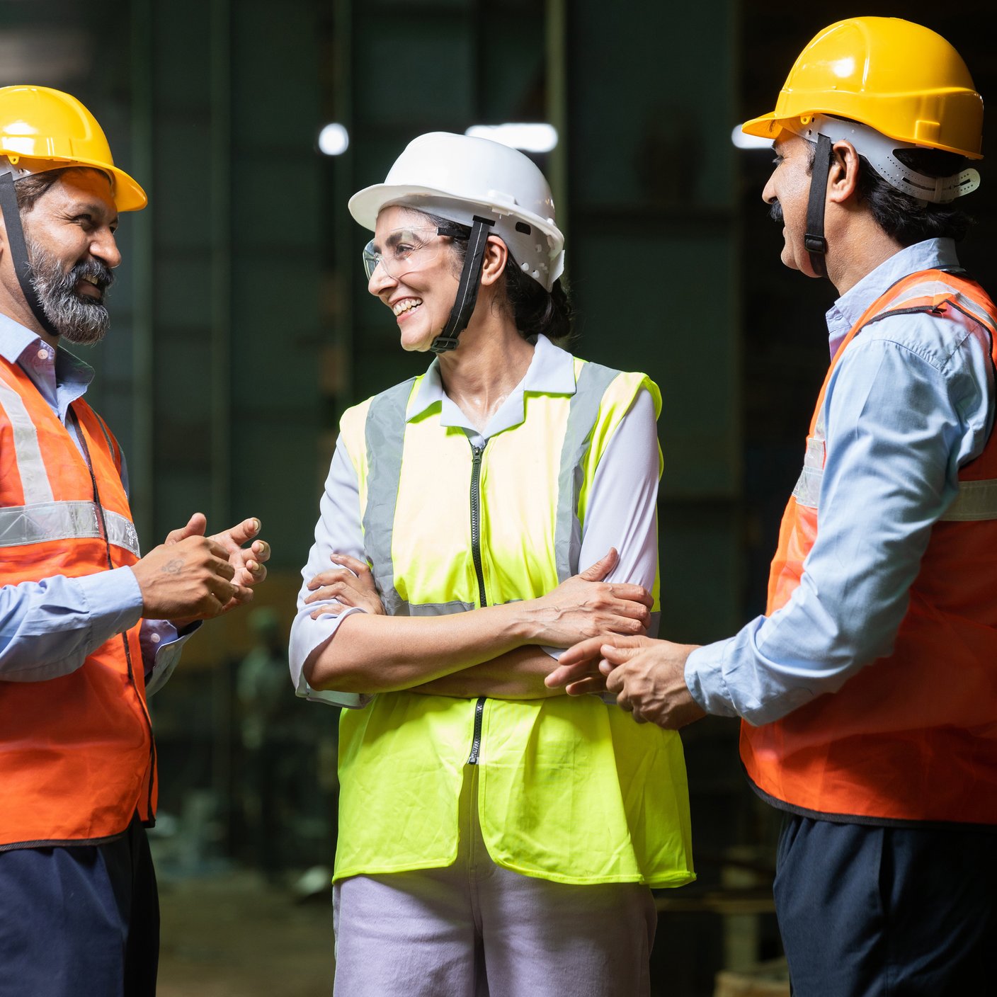 Team of happy indian engineers wearing safety hard hat and vest laughing and talking at industrial factory, skill india concept.