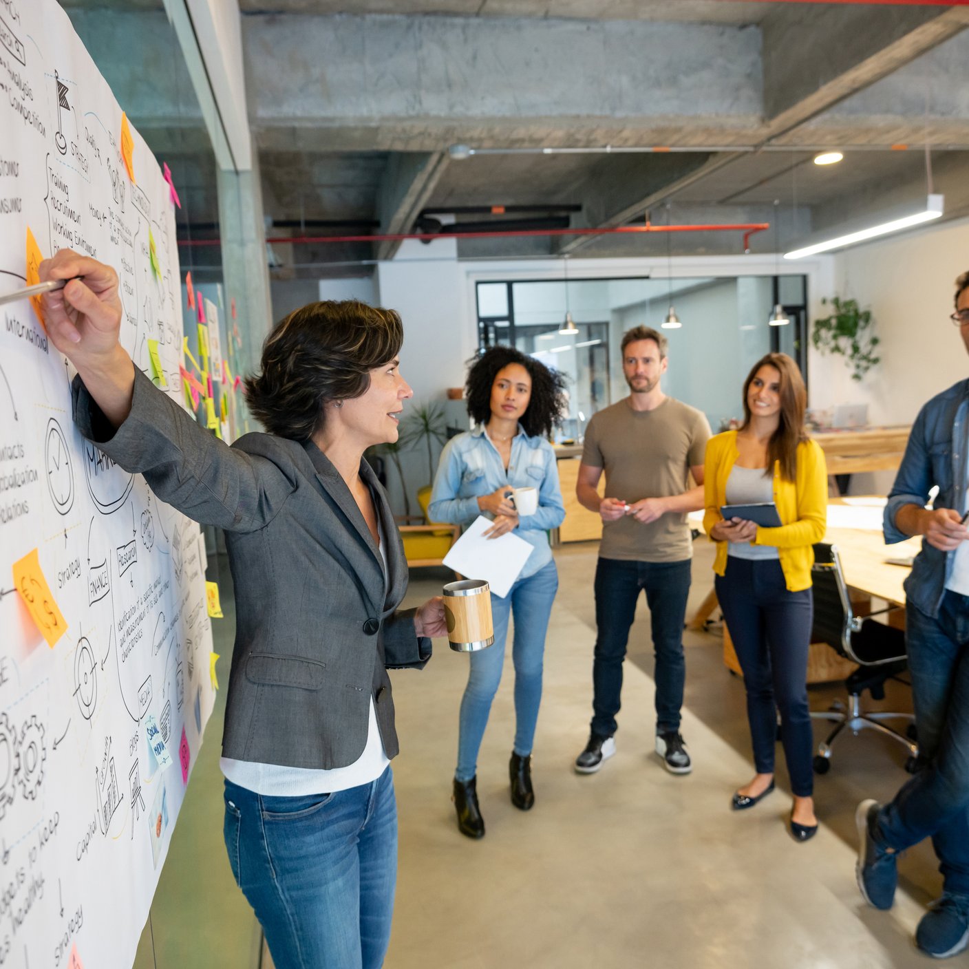 Latin American woman making a business presentation in a meeting at a creative office and pointing to her team her business plan