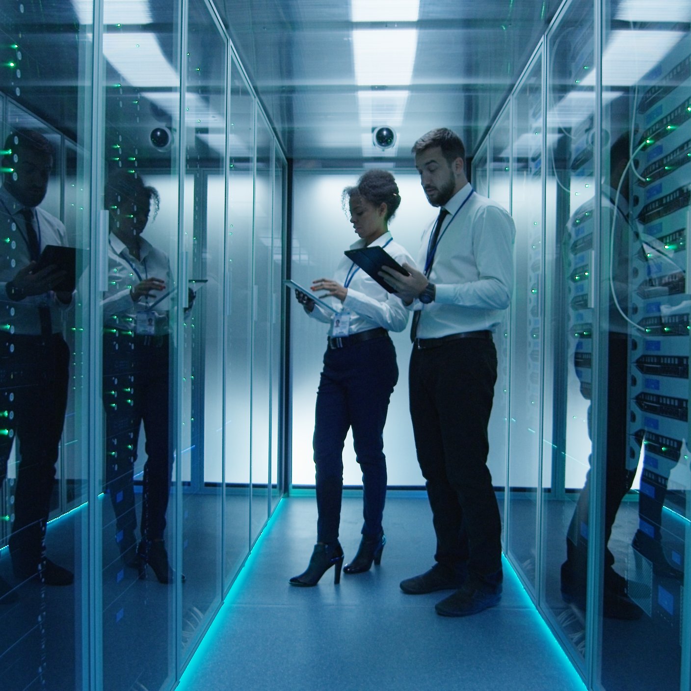 Side view of multiethnic man and woman with tablets coworking in data center server room checking hardware
