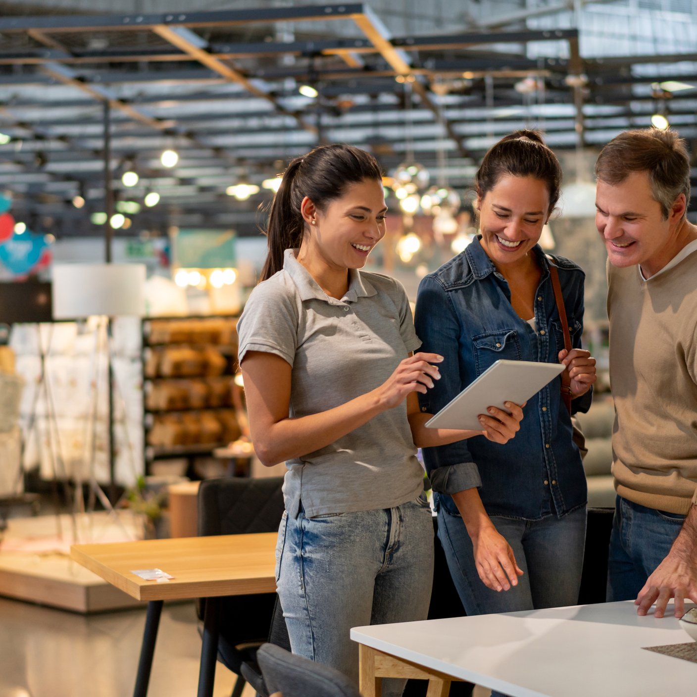 Cheerful sales woman showing a design on tablet to mid adult couple looking for furniture at a home store.