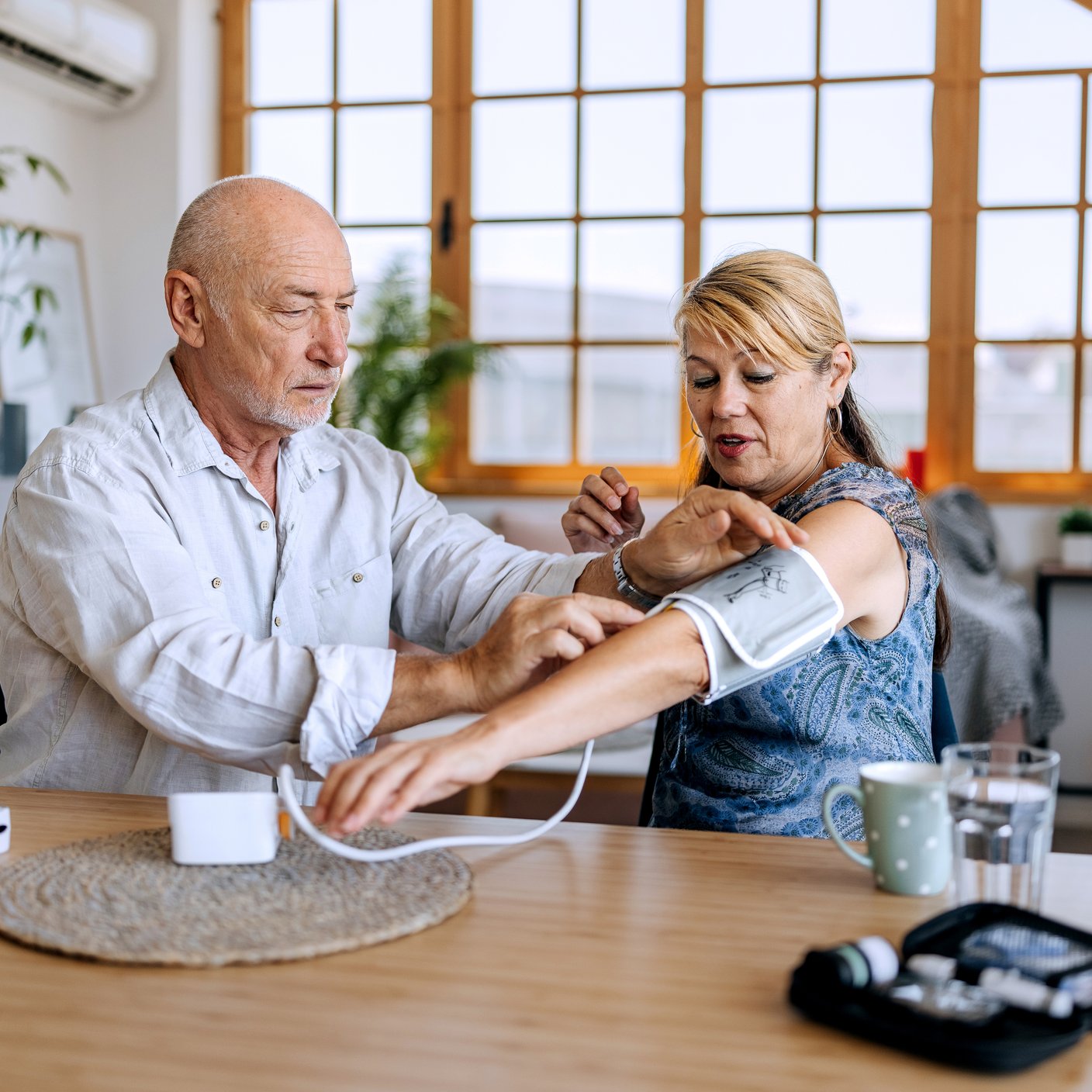 Casually clothed senior couple measuring blood pressure while sitting at the table at home