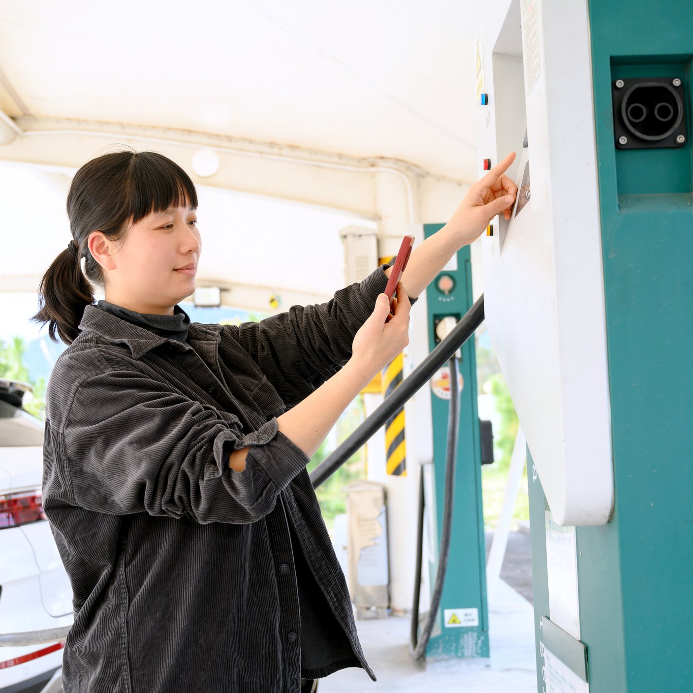 Chinese woman scans QR code on mobile phone to charge new energy car