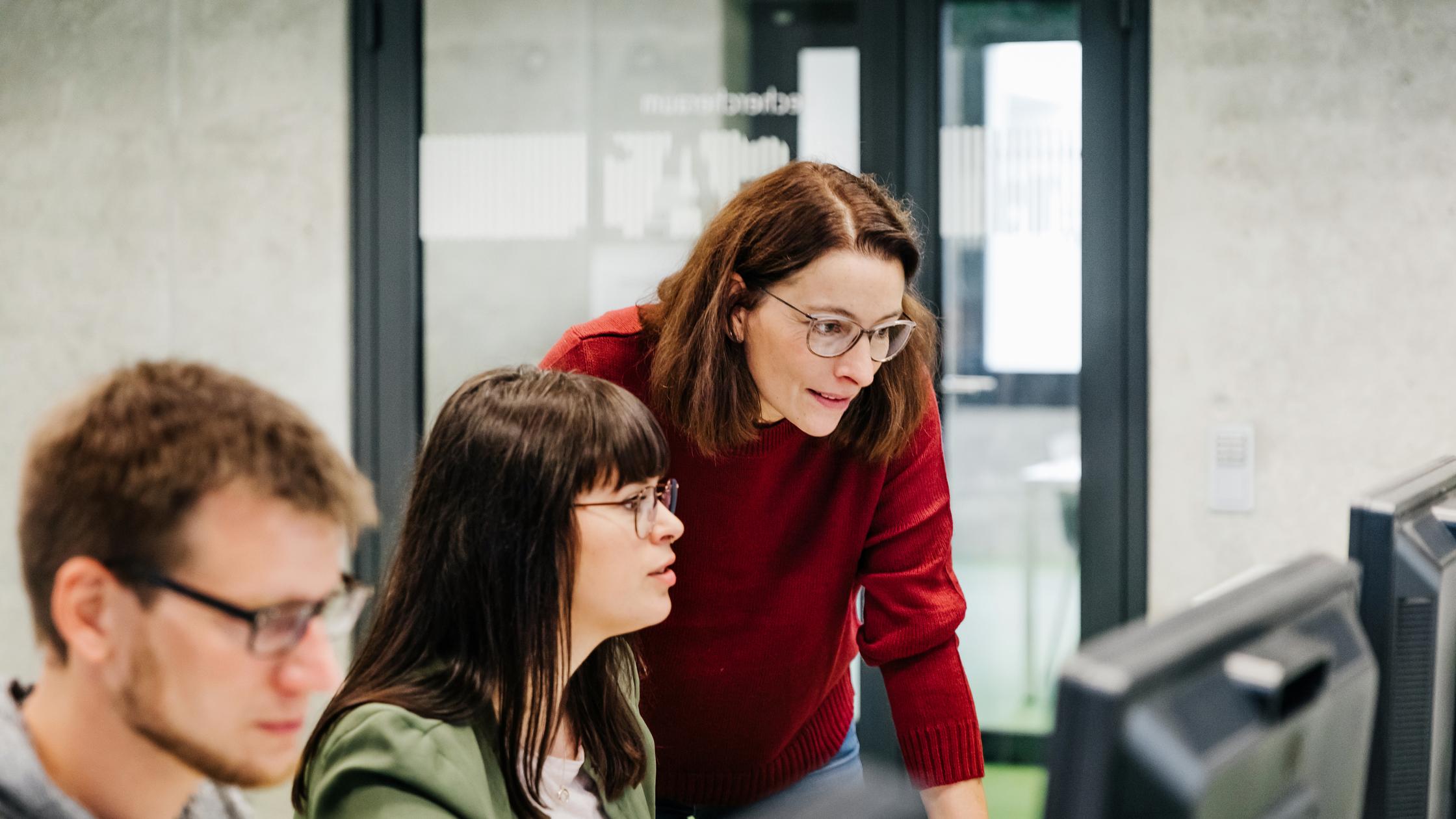 Woman looking over colleagues shoulder at their monitor screen