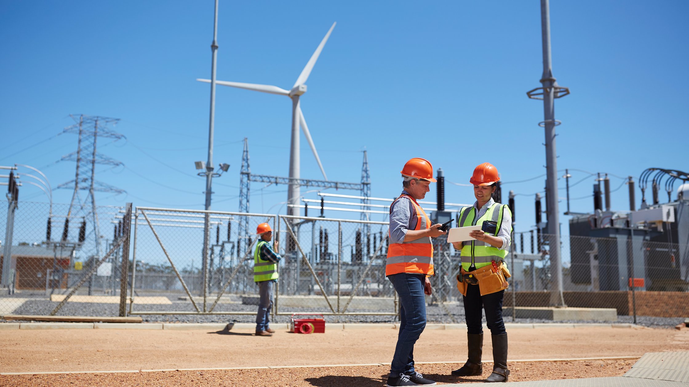 Engineers using digital tablet at sunny wind turbine power plant