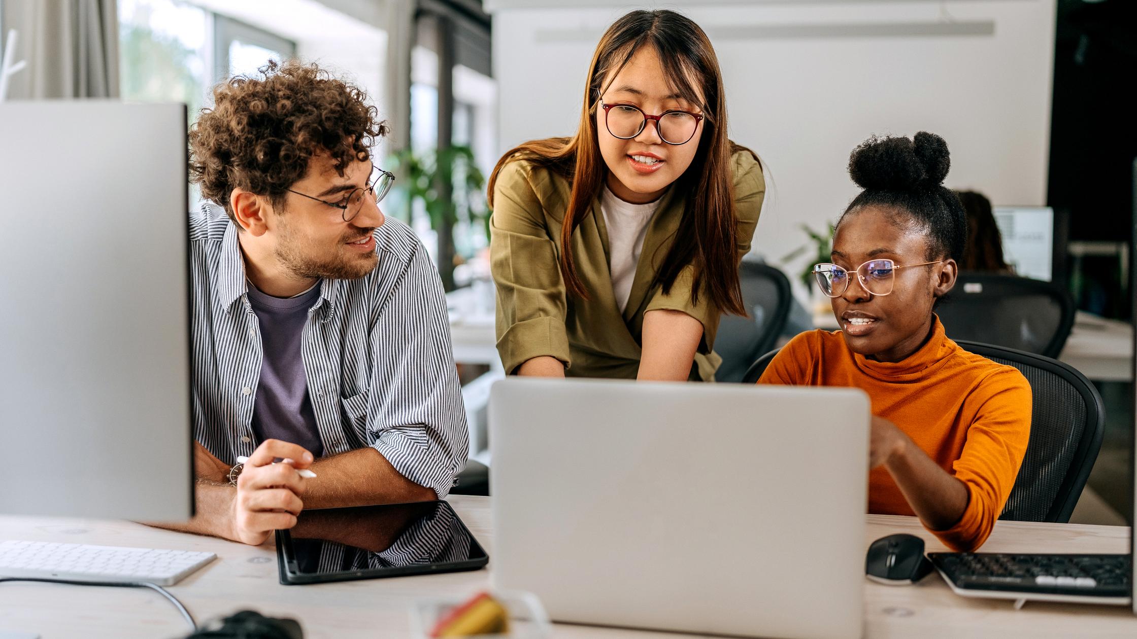 Three coworkers gathered around a laptop