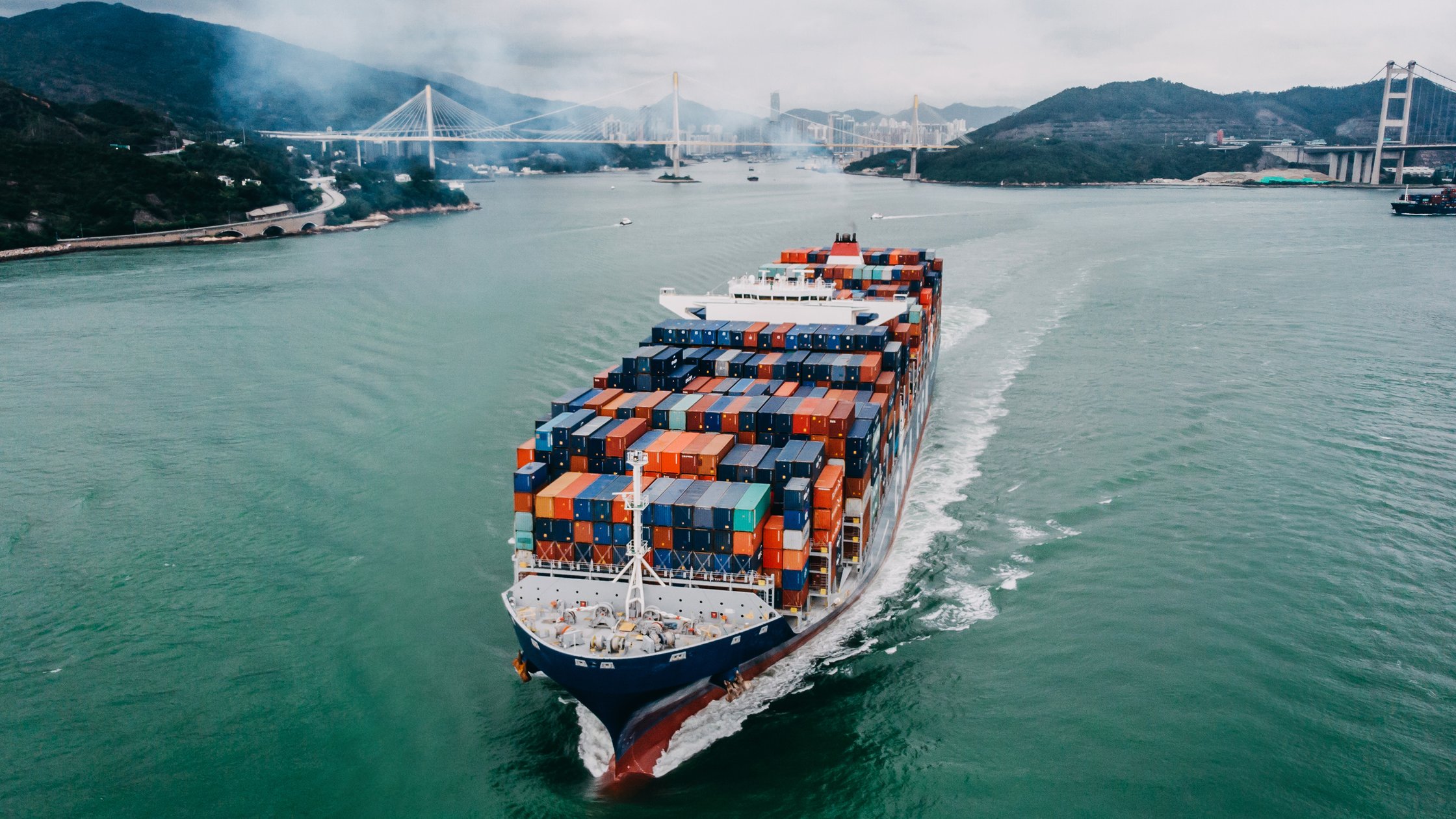 Aerial view of container ship transporting goods sailing across ocean leaving the port. 